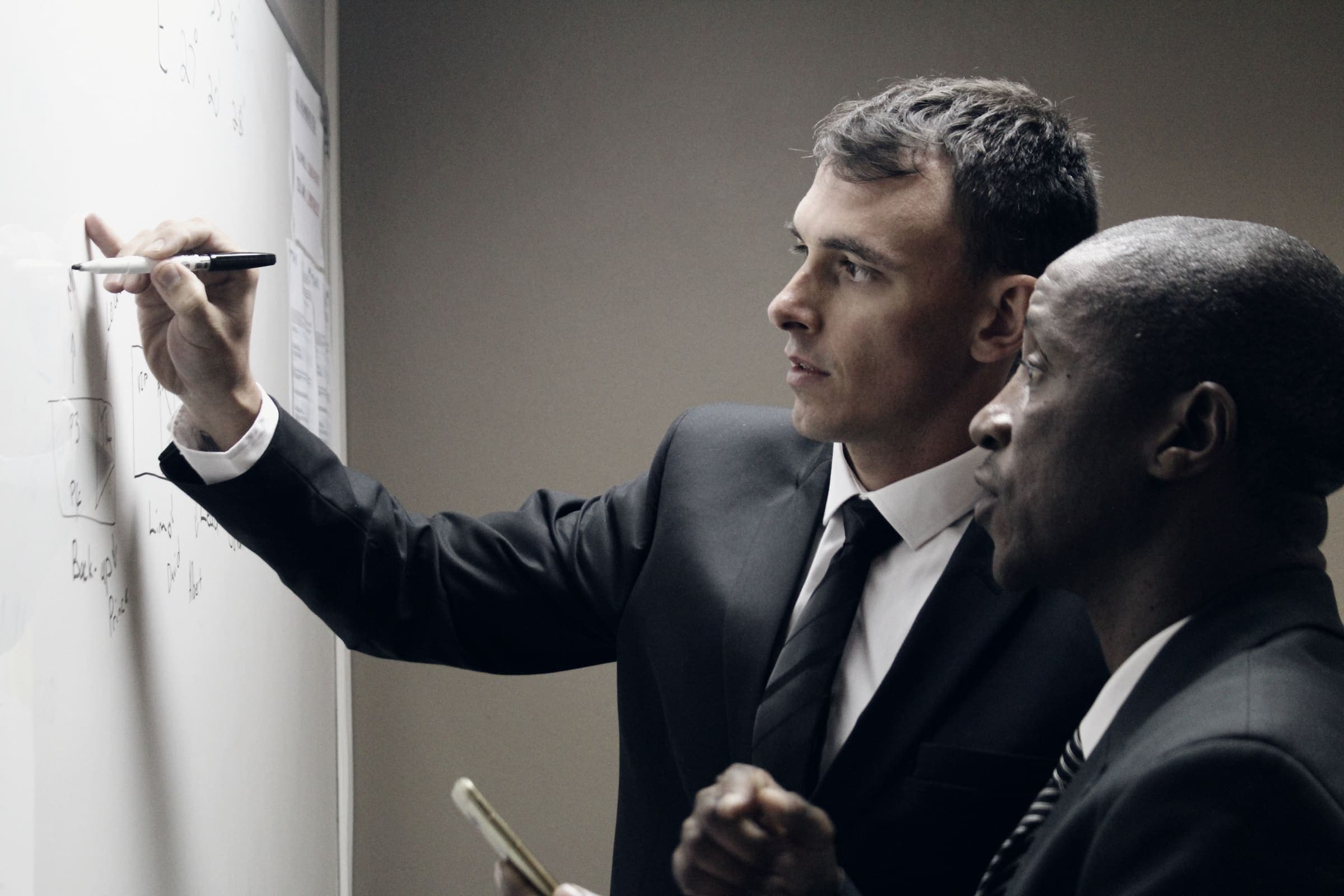 Two suited men at a whiteboard running a risk assessment