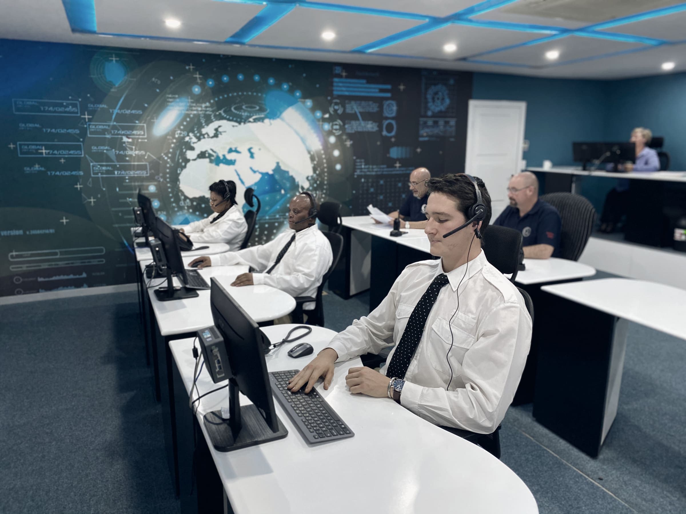 Control room operators in white shirts and headsets, world-map wall graphic (2021 fit-out)