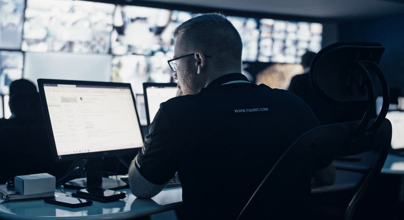 Operator in TSU shirt at desk facing CCTV video wall (newer control room)