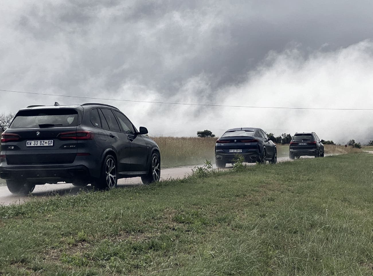 Three black SUVs in convoy on a rural road