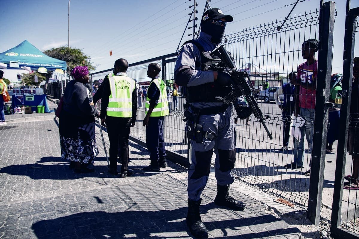 Armed officer at an event perimeter fence, guards in hi-vis