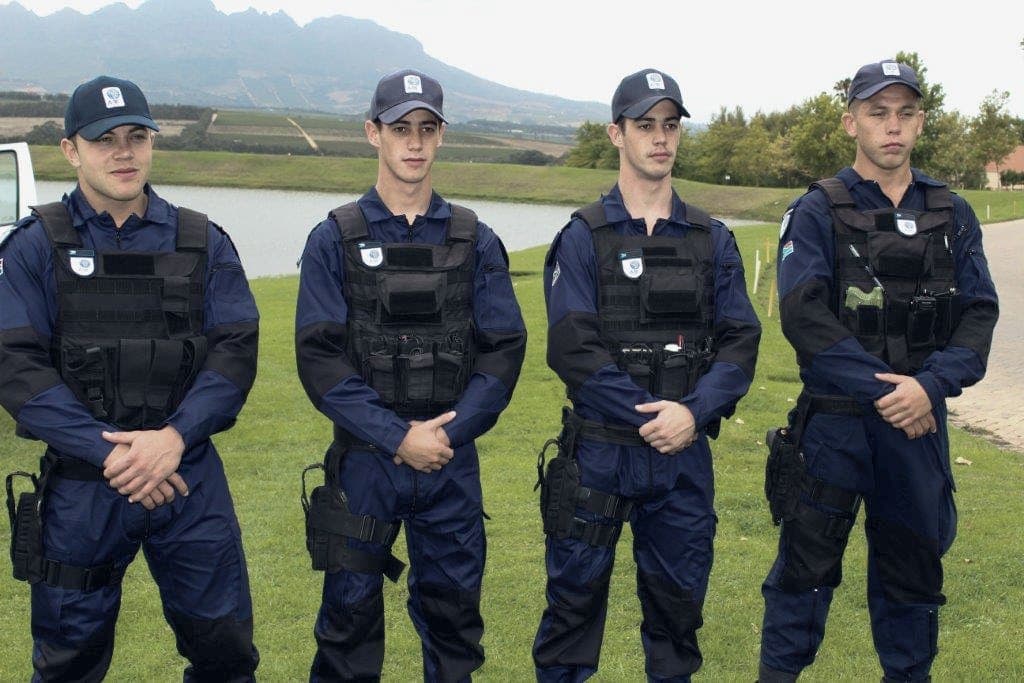 Four uniformed officers in vests and caps on a lawn, mountain behind
