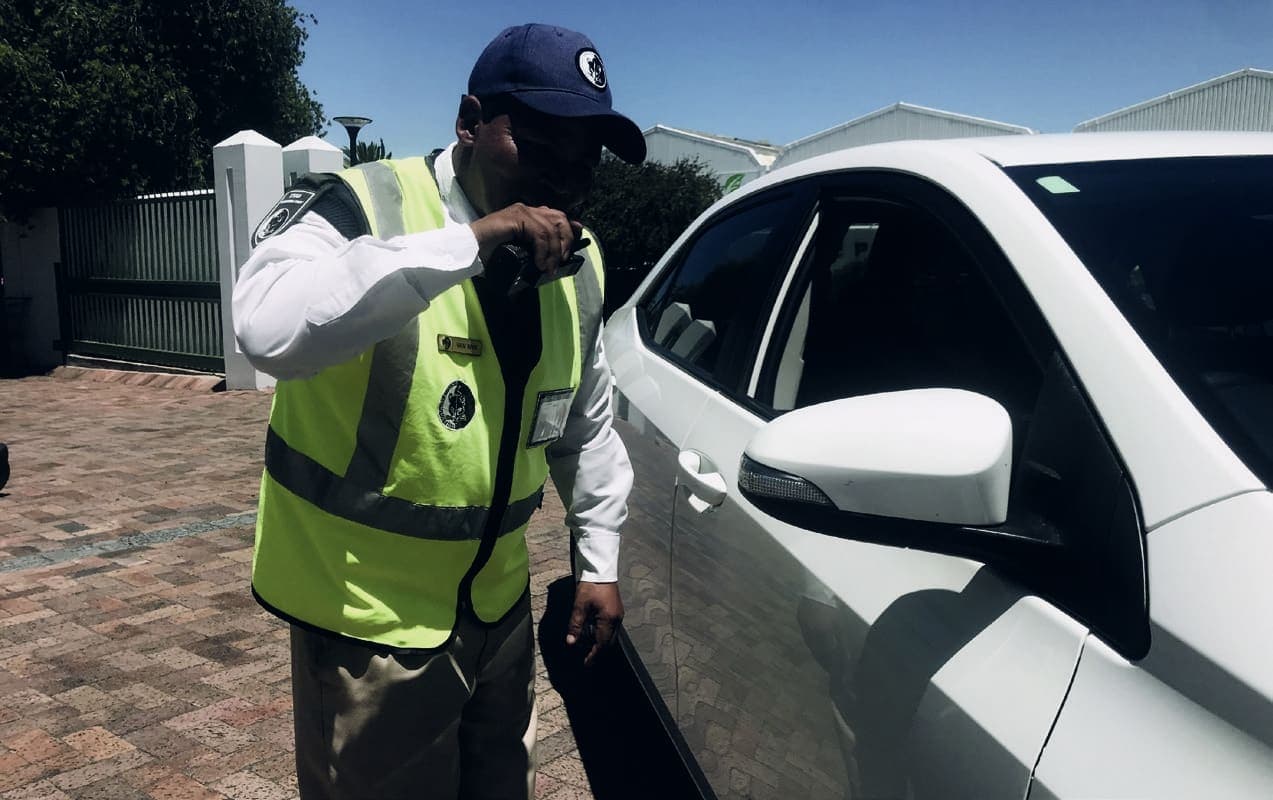 Guard in hi-vis on radio checking a white car (alt angle)