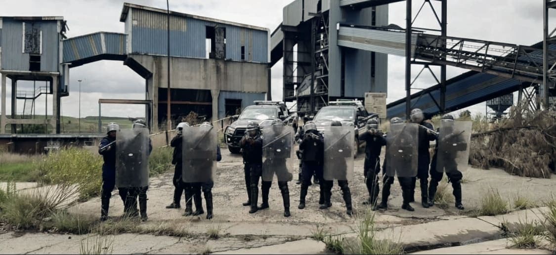 Riot/APT shield line at a mine/industrial site (very wide, small)