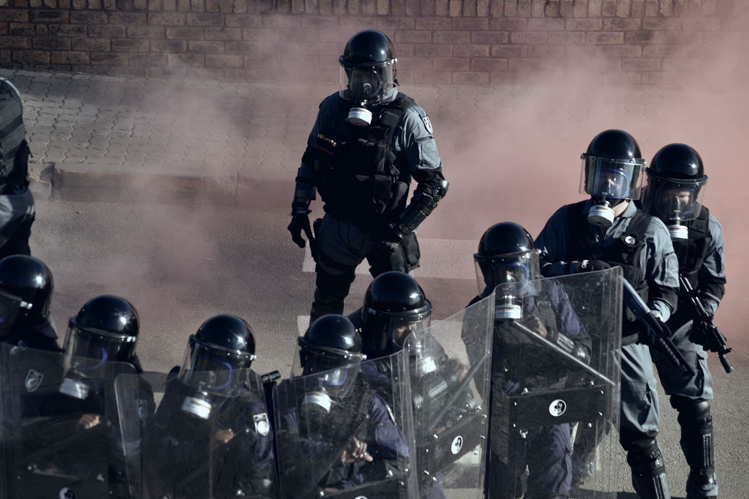 Riot unit in helmets, gas masks and shields in pink smoke