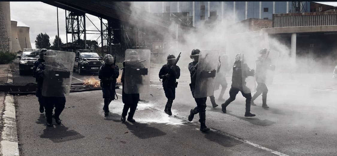 Riot team advancing in street through smoke (very wide, small)