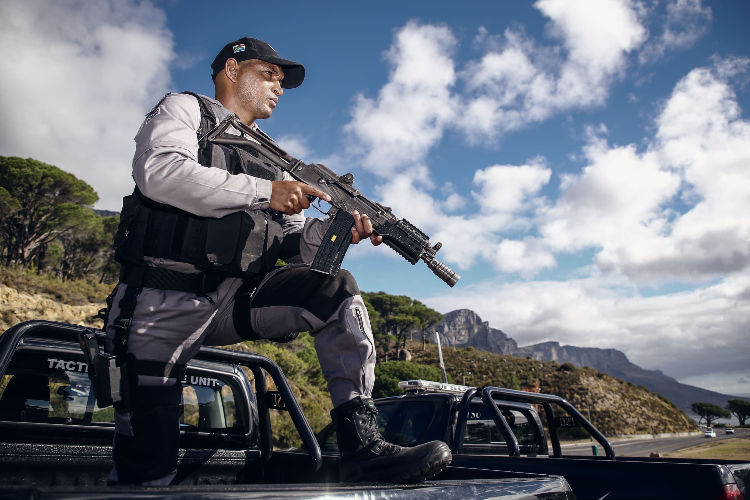 Tactical officer with rifle crouched on vehicle, Cape mountains and sky