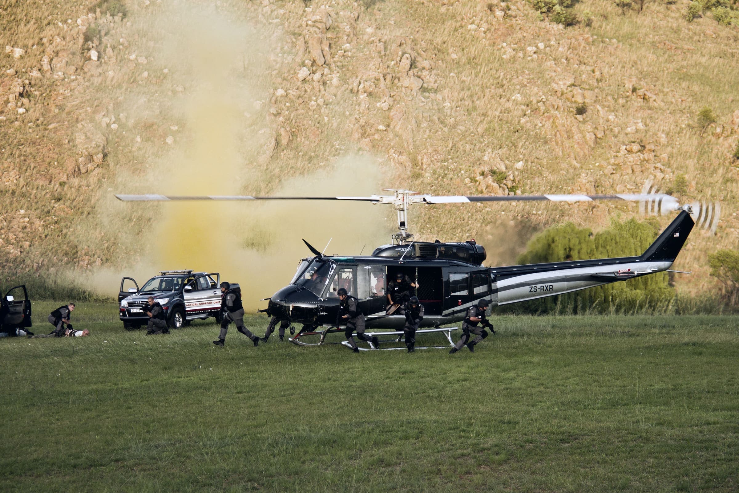 Helicopter landed beside branded tactical vehicles, team deploying through coloured smoke
