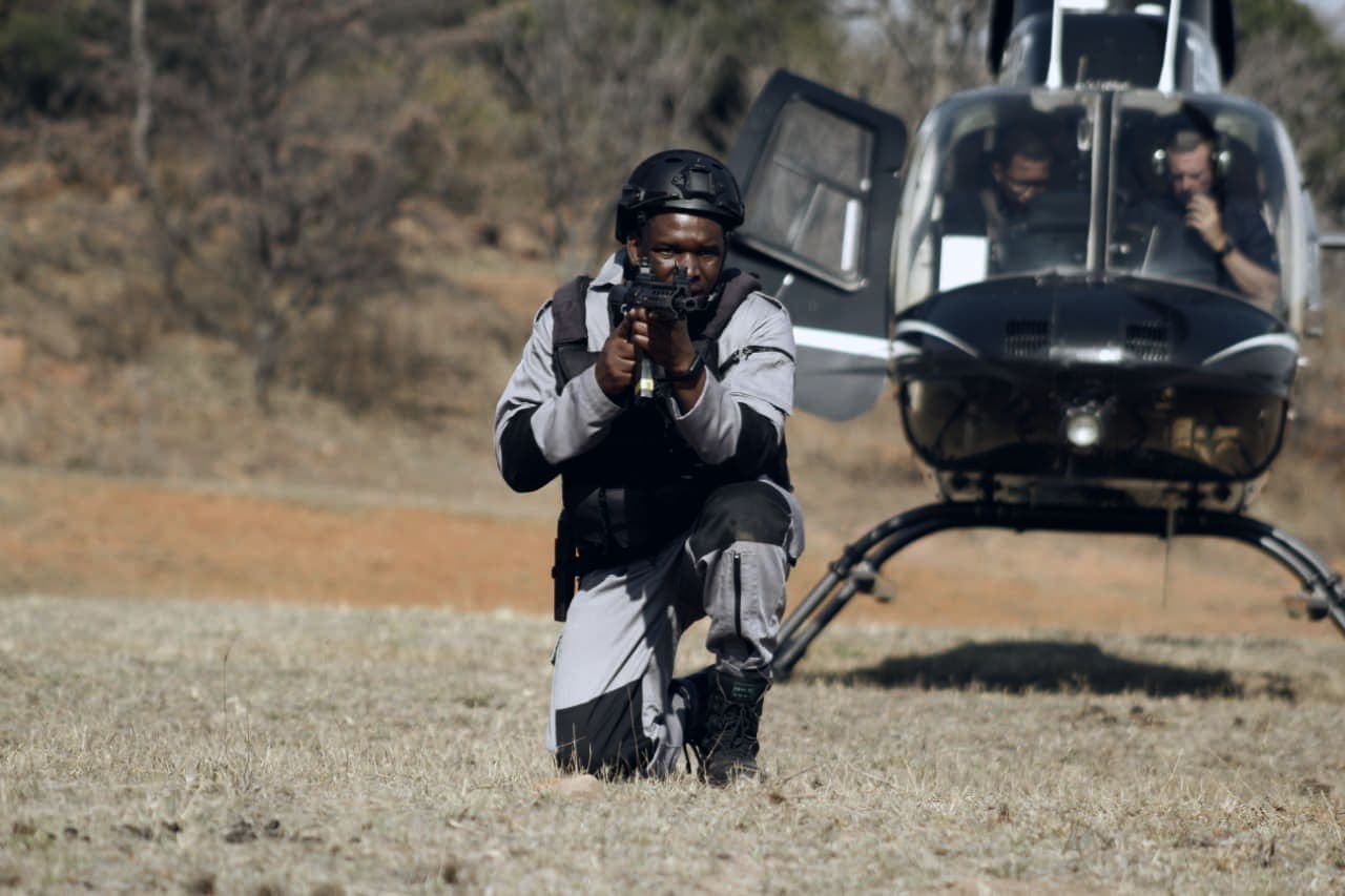 Tactical officer aiming rifle, kneeling in front of a landed helicopter