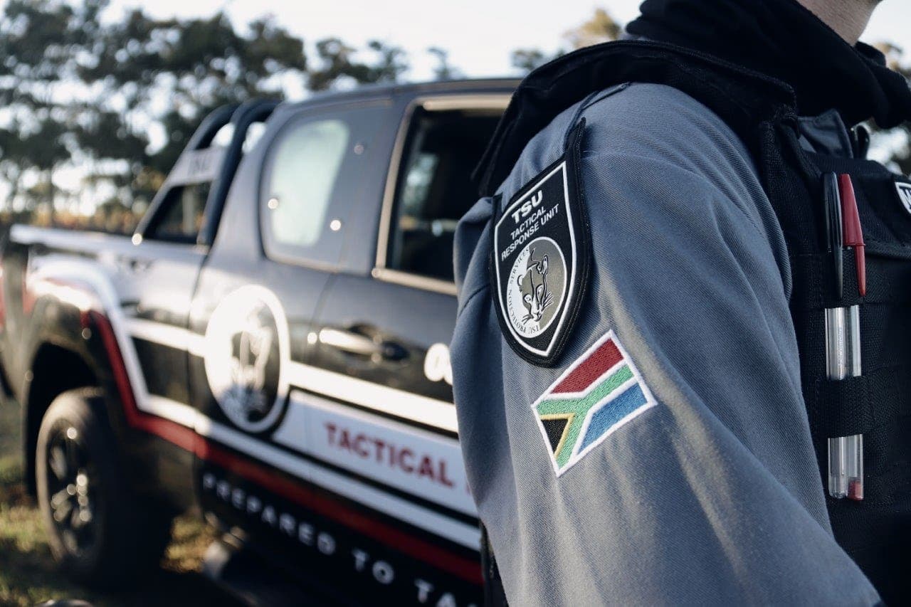 Close-up of shoulder: TSU patch and SA flag, branded TACTICAL vehicle behind